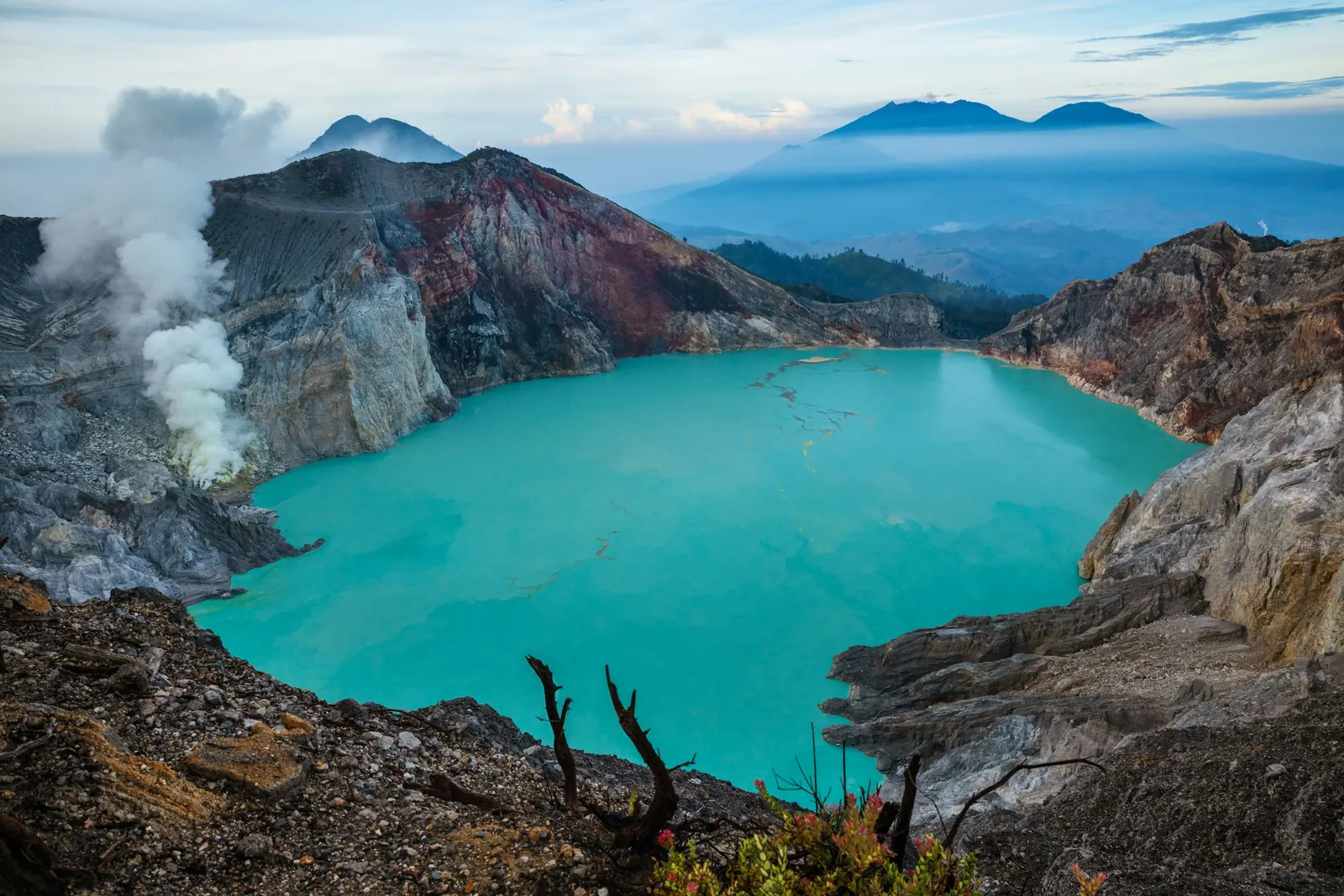 The turquoise acid lake inside the Kawah Ijen crater, sulphur smoke rising on the left