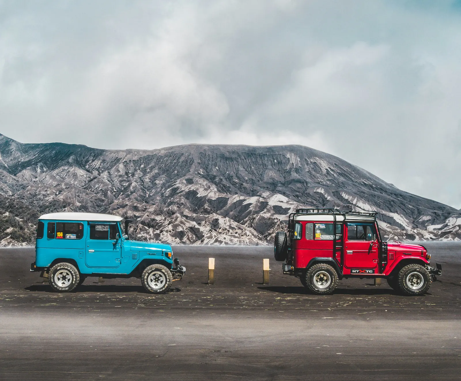 A blue and a red 4x4 jeep on the Bromo sea of sand, the crater wall behind