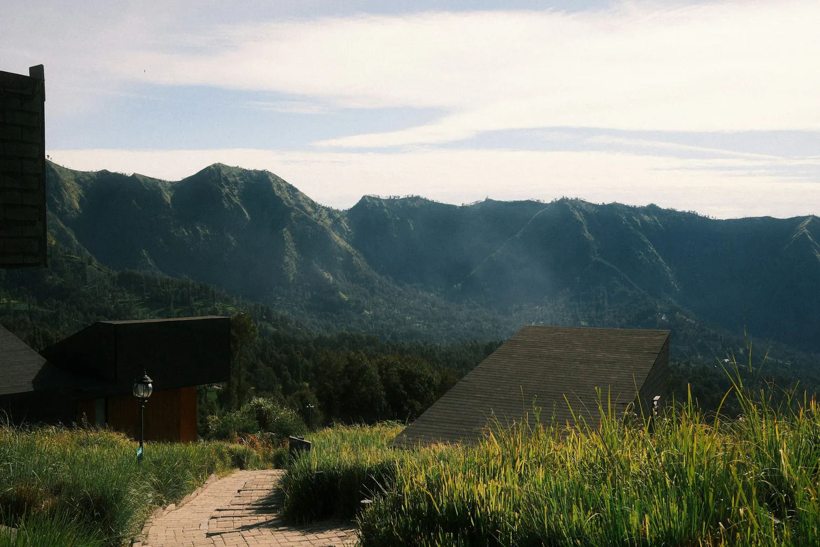 Wooden cabins on a grassy slope at Cemoro Lawang, the caldera wall behind