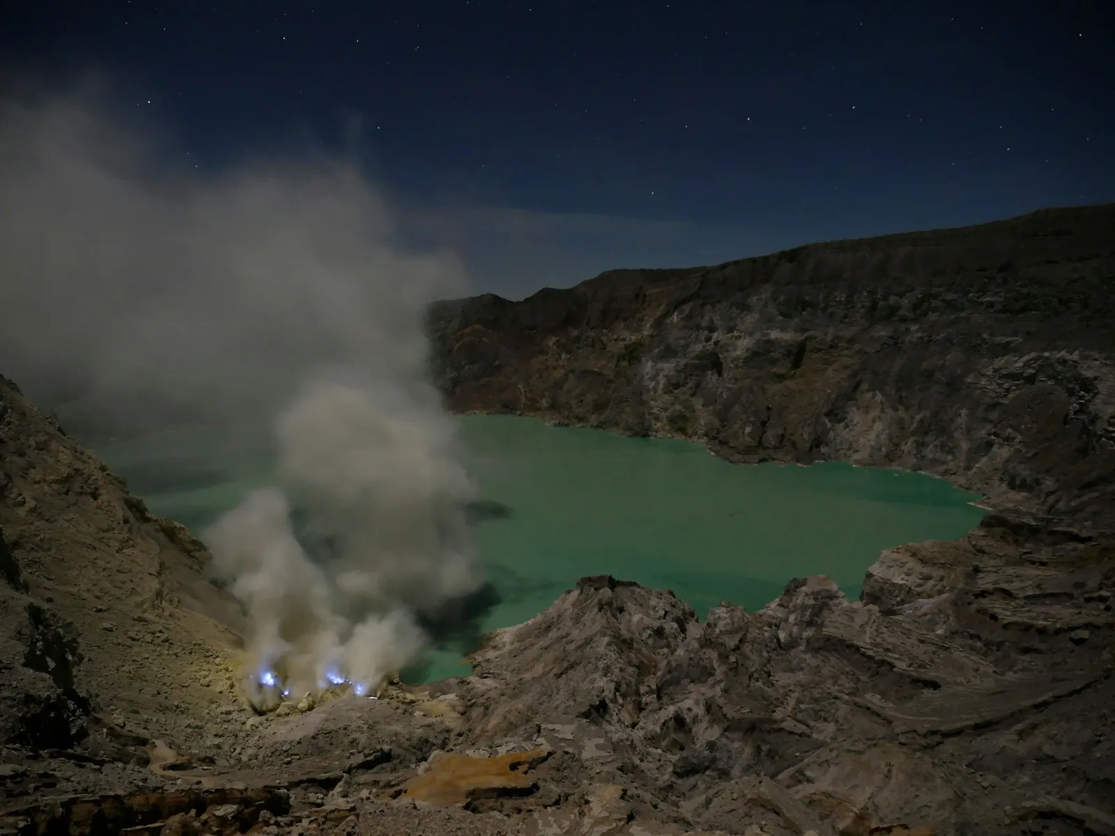 Blue sulphur flames burning at night beside the Kawah Ijen crater lake